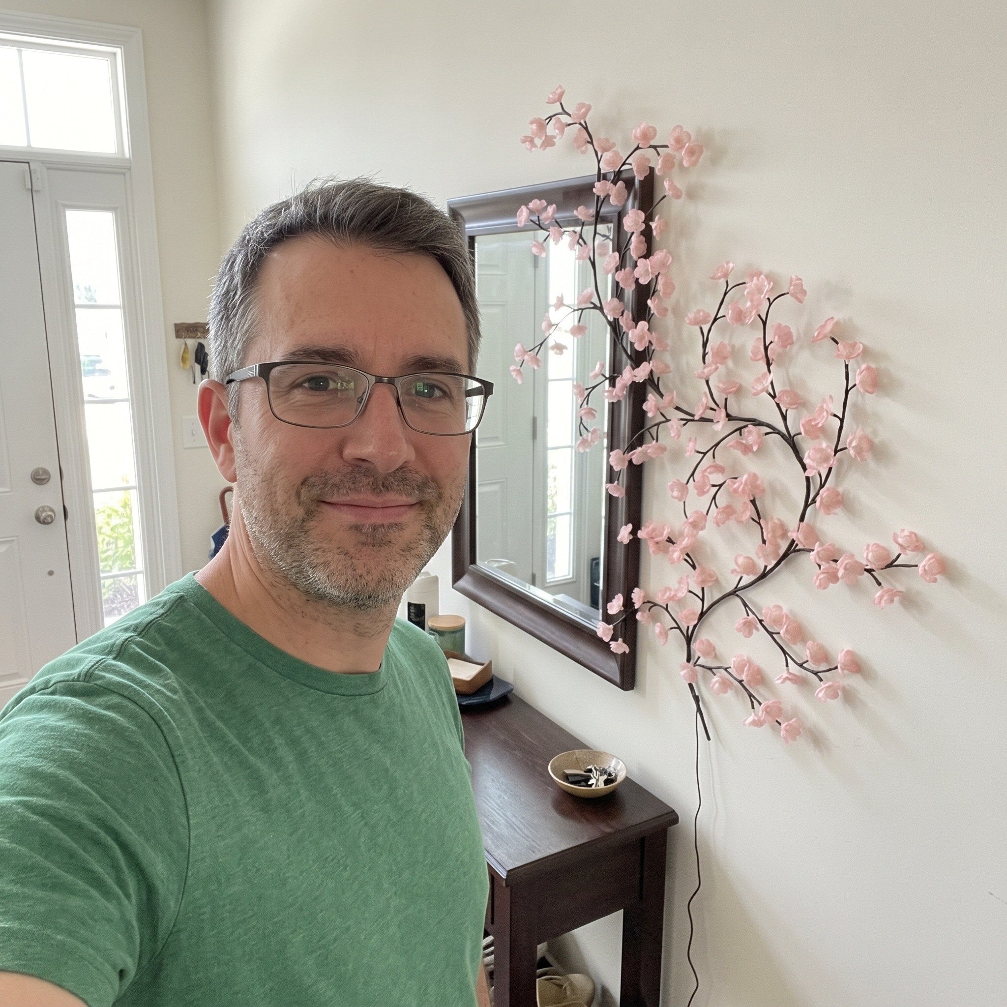 Man taking an entry hall selfie by pink blossom vine lights
