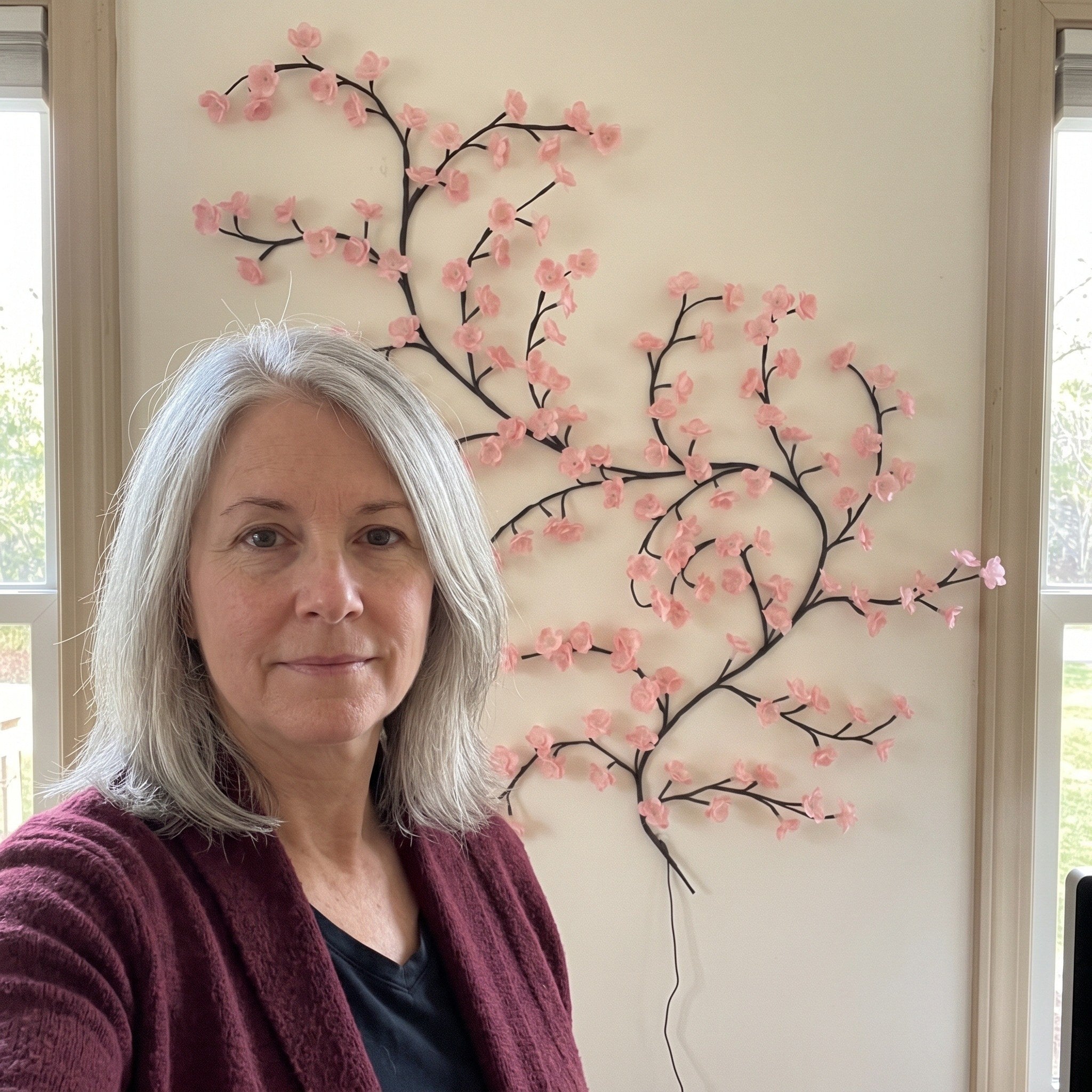 Woman taking a window-side selfie by pink blossom vine lights