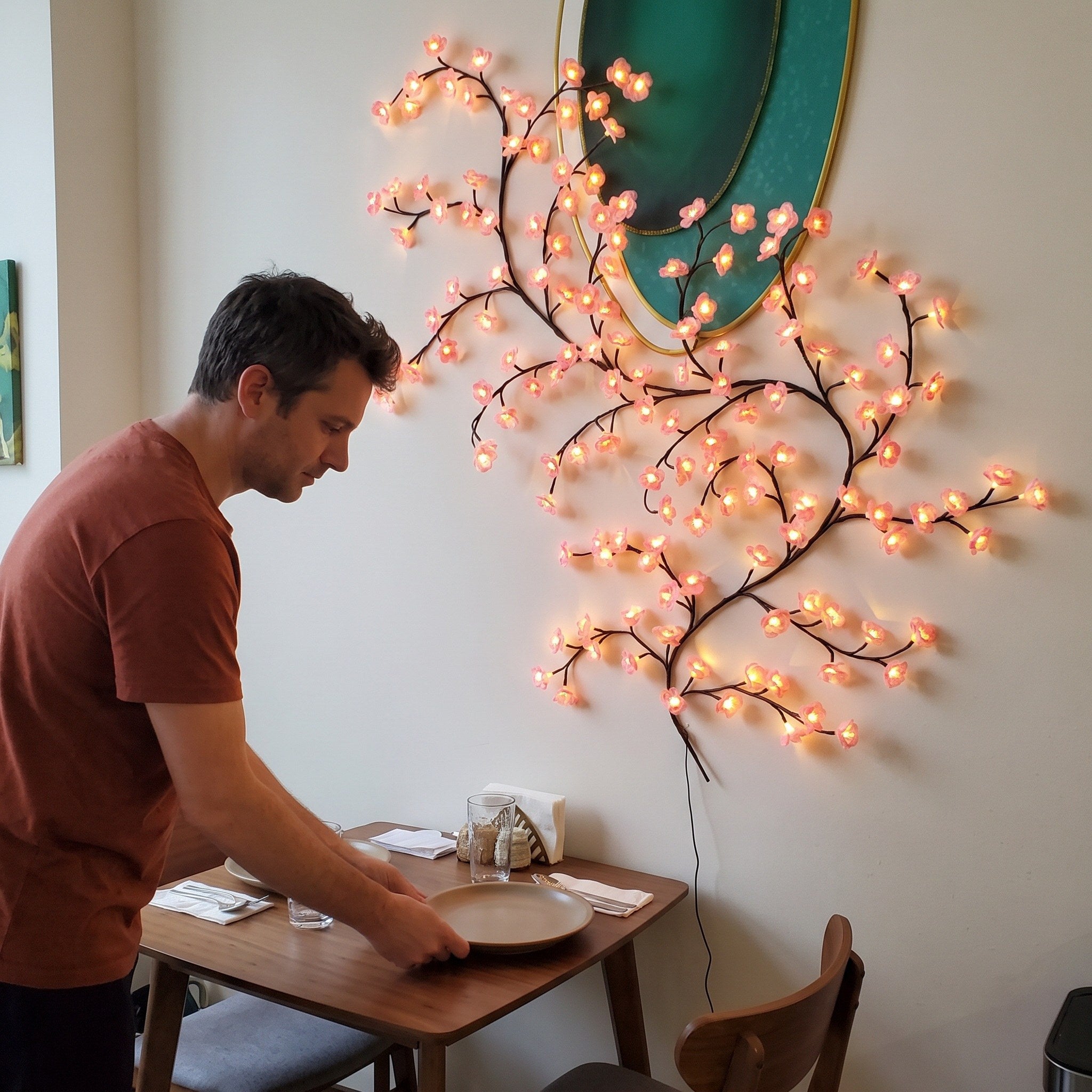 Man setting a dining table beside pink blossom vine lights