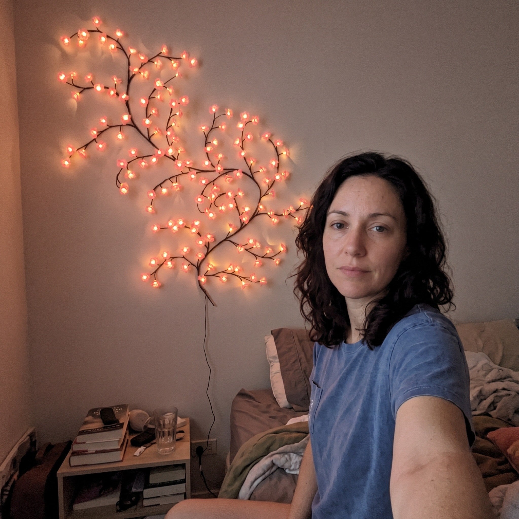 Woman taking a selfie by bedside pink blossom vine lights